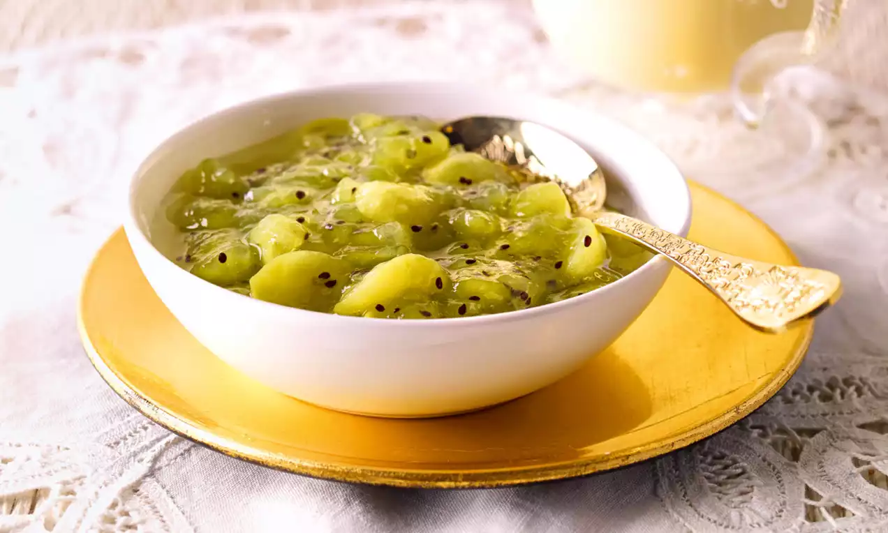 Leuchtend grün-gelbes Kiwi-Trauben-Kompott mit sichtbaren schwarzen Kiwi-Kernen, serviert in einer weißen Schale auf goldenem Unterteller