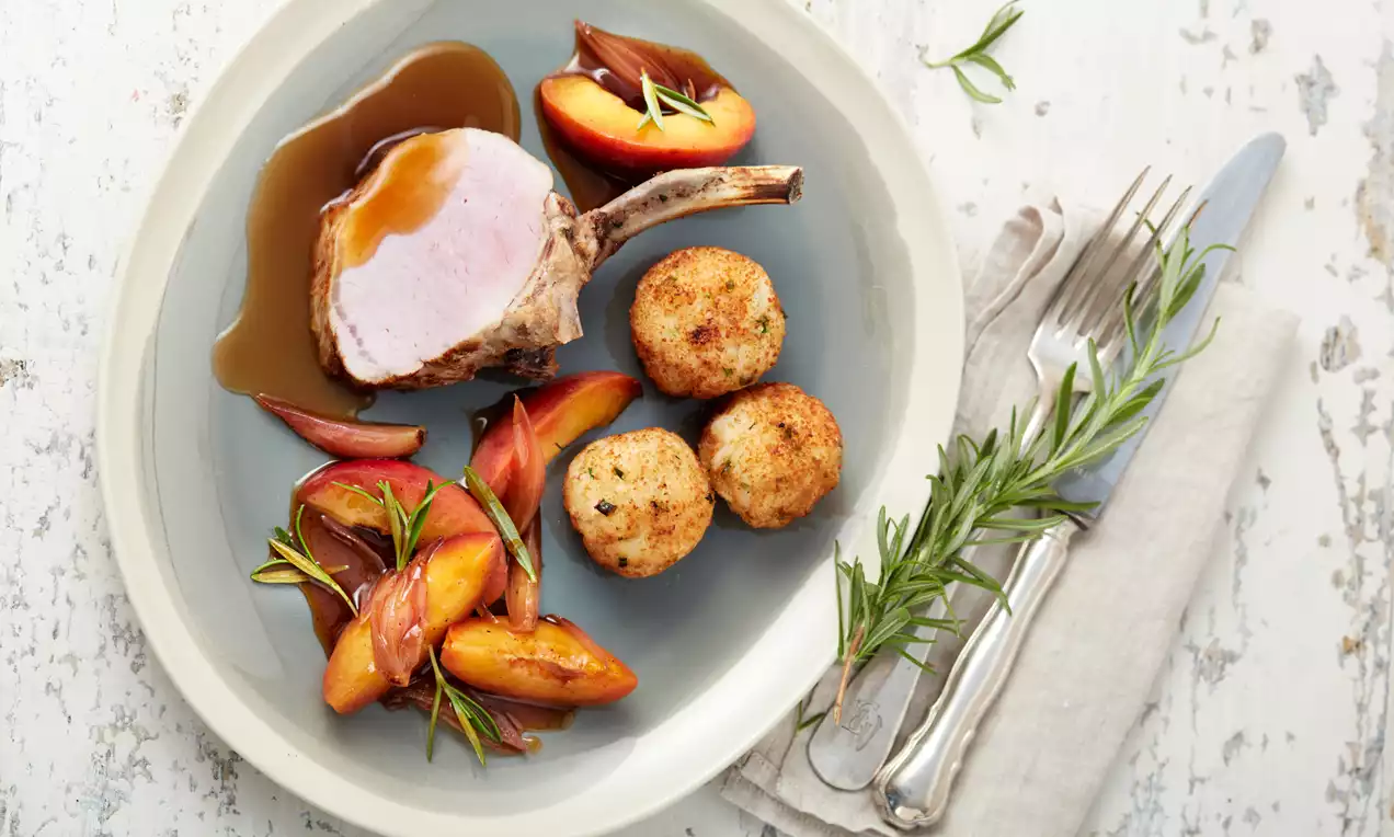 Saftiges Karree vom Duroc-Schwein mit rosa Kern, goldbraune Risottobällchen und glänzende Rosmarin-Nektarinen auf grauem Teller