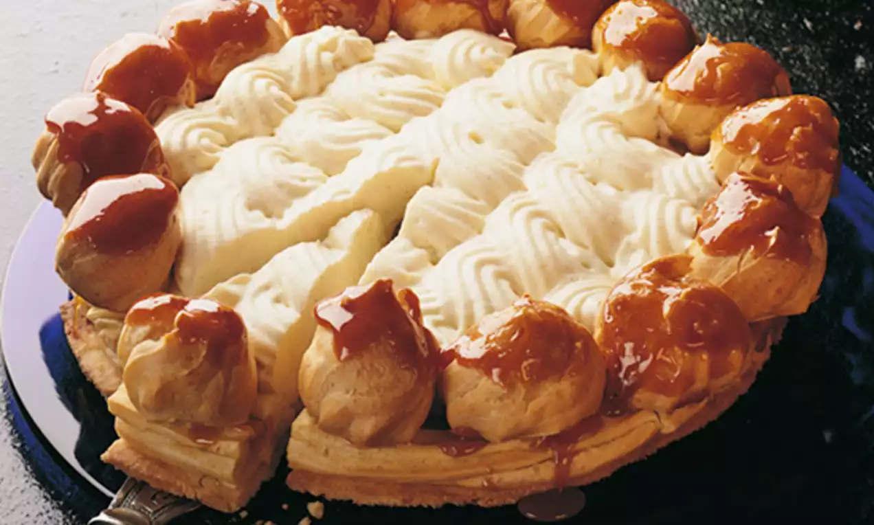 Torte St. Honoré mit goldbraunen Windbeuteln an einem karamellglänzenden Ring, Vanillecreme und weißen Sahnetupfen dekoriert