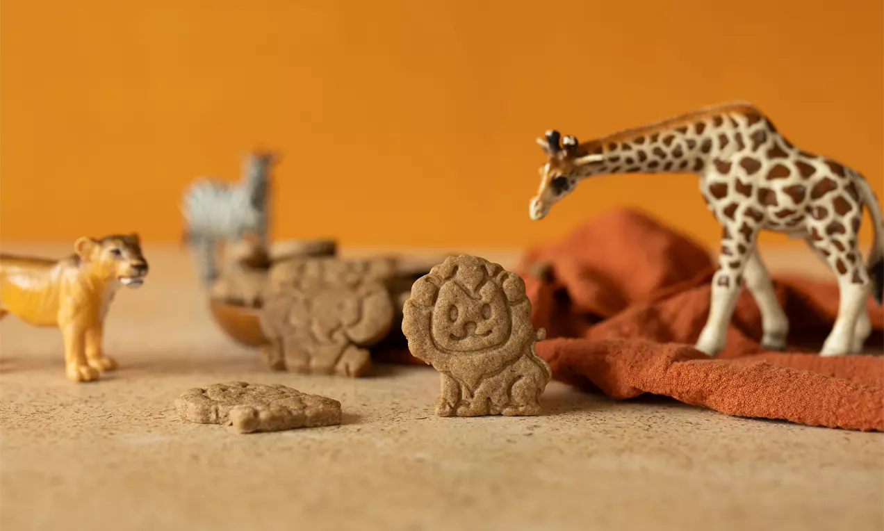 Biscuits Speculoos en forme d'animaux safari, texture gravée, posés sur une table beige avec figurines et tissu orange brûlé