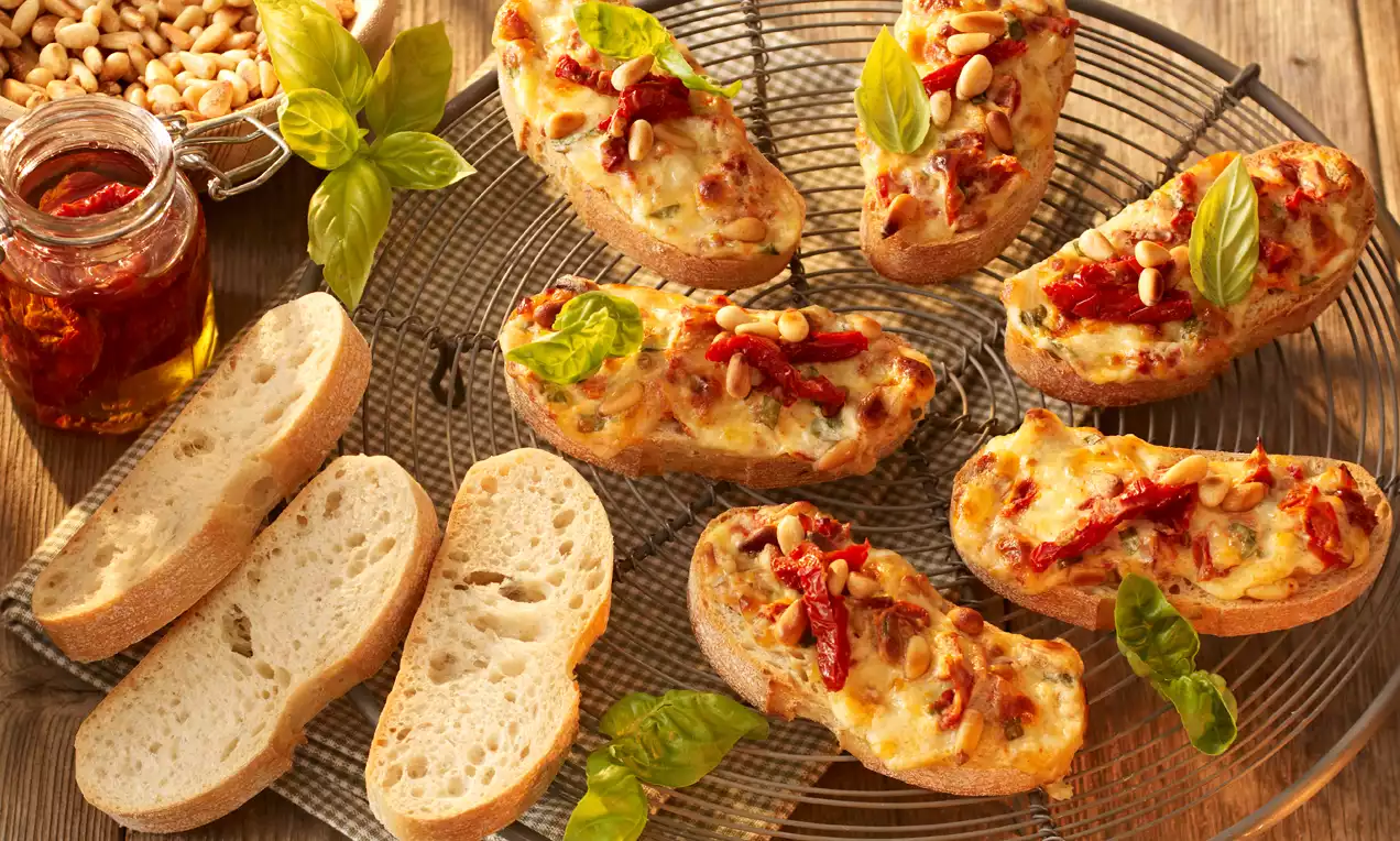 Goldbraun überbackenes Basilikum-Ciabatta mit geschmolzenem Käse, getrockneten Tomaten, Pinienkernen und frischen Basilikumblättern auf einem Rost