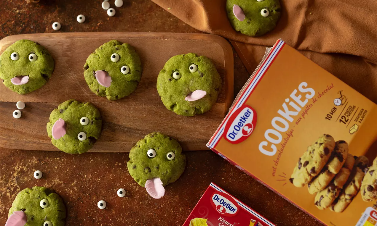 Cookies verts rondes à la surface moelleuse, décorés d’yeux en sucre et de langues rose, disposés sur une planche en bois