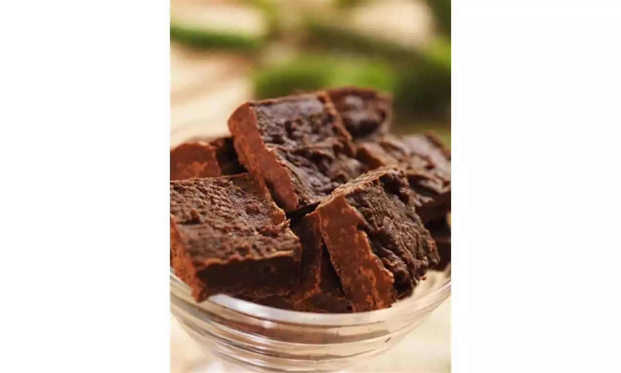 Biter av mørkebrun fudge med ru overflate stablet i en gjennomsiktig glasskål, med uskarp grønn bakgrunn