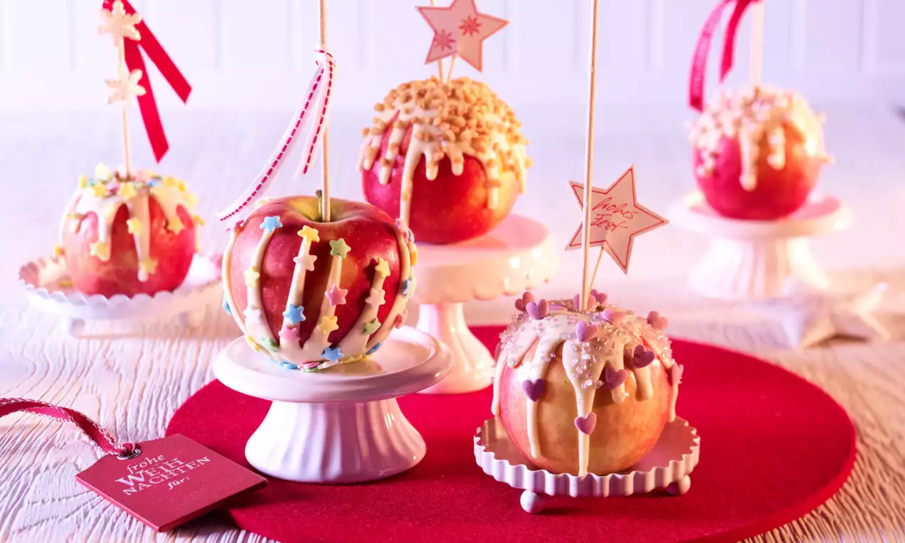 Crvene jabuke na bijelim postoljima, obložene bijelom glazurom, posute raznobojnim dekoracijama i ukrašene trakama i zvjezdicama