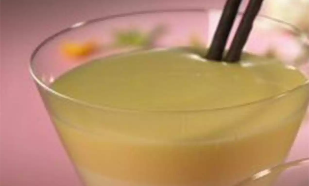 Gladde, lichtgele wijnvla in een transparant glas, met een subtiele laag en chocolade-stokjes op een roze achtergrond