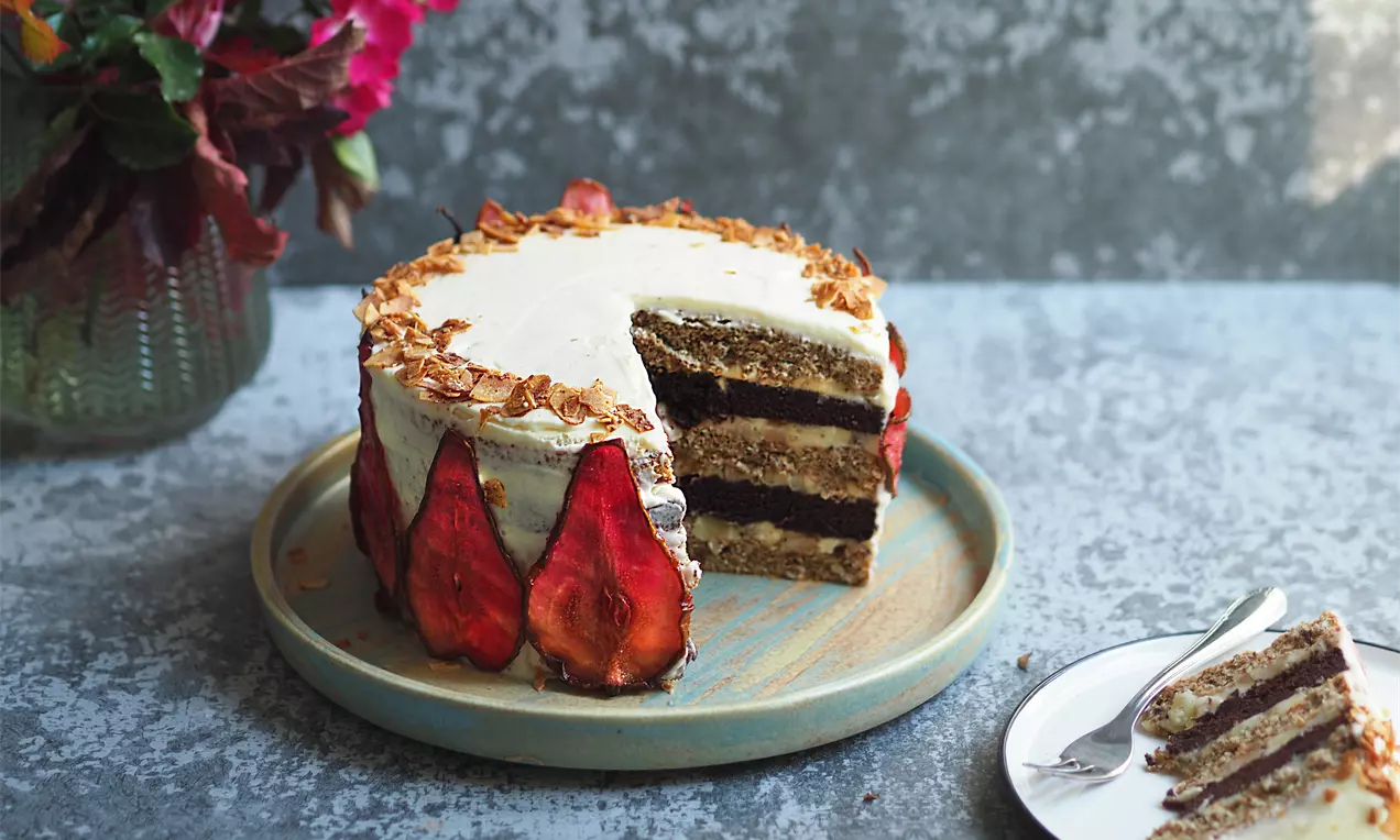 Торта с тъмнокафяви орехови пластове, покрити с светъл крем, декорирана с резени сушени круши и ядки върху керамична чиния