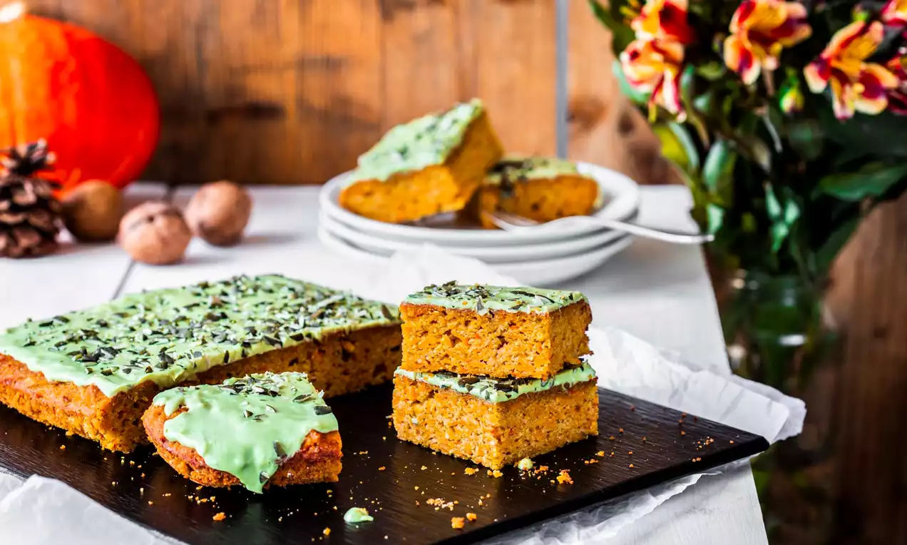 Zeltaini oranži ķirbju batoniņi ar zaļu glazūru un tumšās šokolādes skaidiņām ir izkārtoti uz tumša dēļa dabīgā gaismas fonā