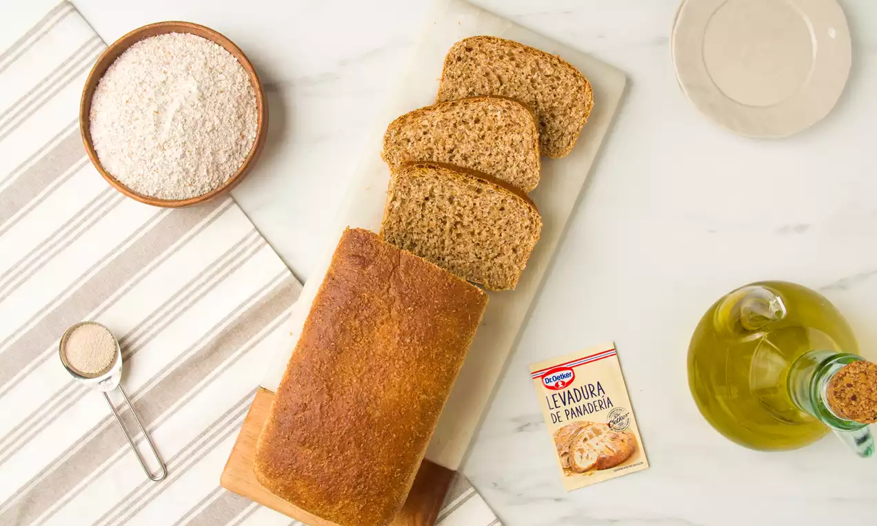 Pan integral de superficie dorada y textura compacta, con rebanadas finas sobre una tabla de mármol, rodeado de harina y aceite