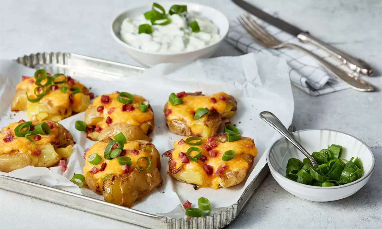 Goldbraune Kartoffeln mit geschmolzenem Käse und knusprigen Speckwürfeln, garniert mit grünen Frühlingszwiebeln auf Backpapier in einer Metallform