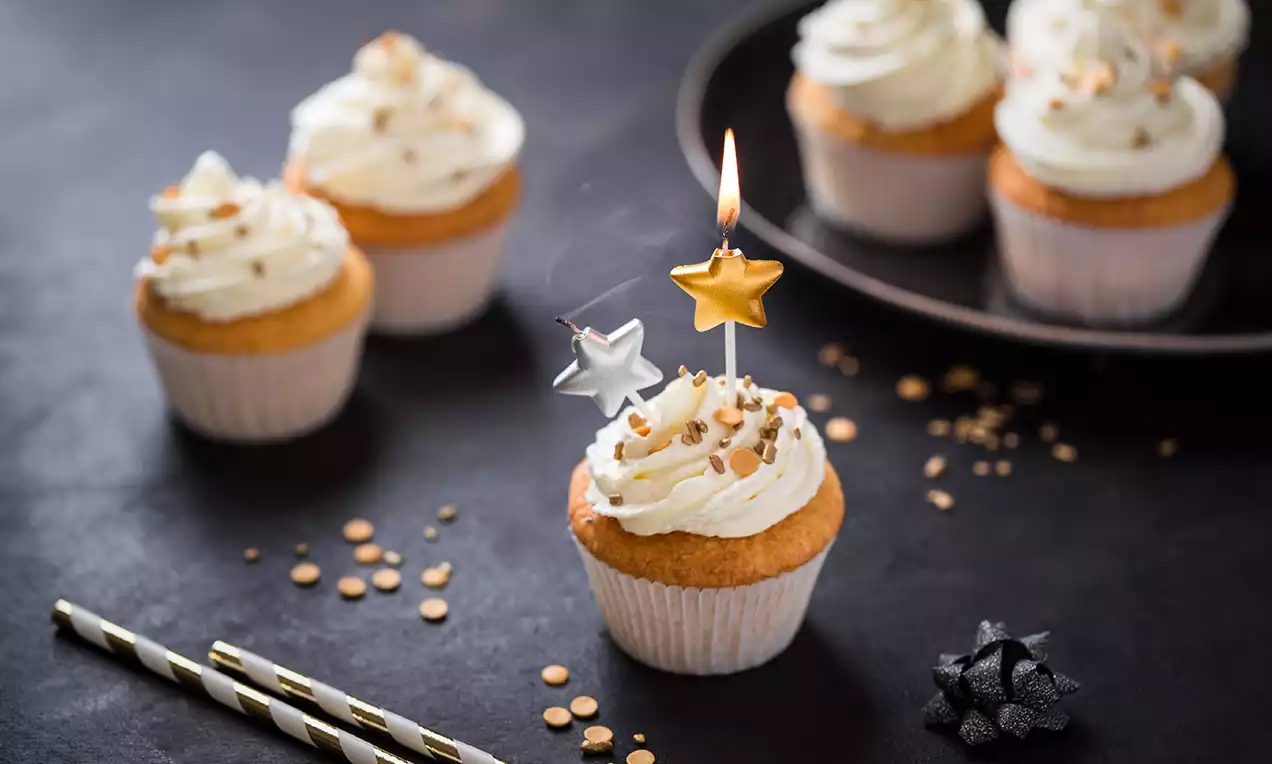 Zitronen Cupcakes mit goldenen Zuckerstreuseln auf weißer Cremetopping, dekoriert mit silbernem und goldenem Stern auf dunklem Hintergrund