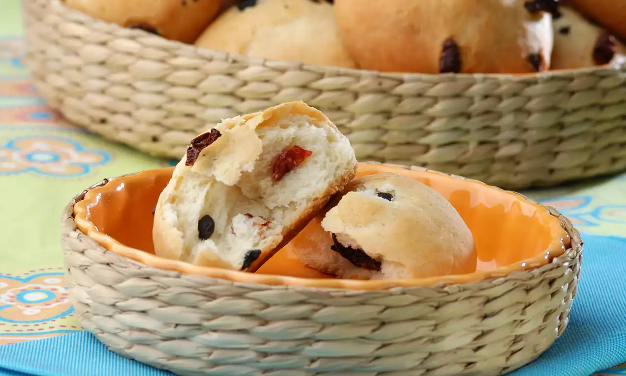 Küçük, yuvarlak zeytinli ekmekçikler açık renkli hasır bir sepette, canlı turuncu bir kasede ve mavi bez üzerinde düzenlenmiş