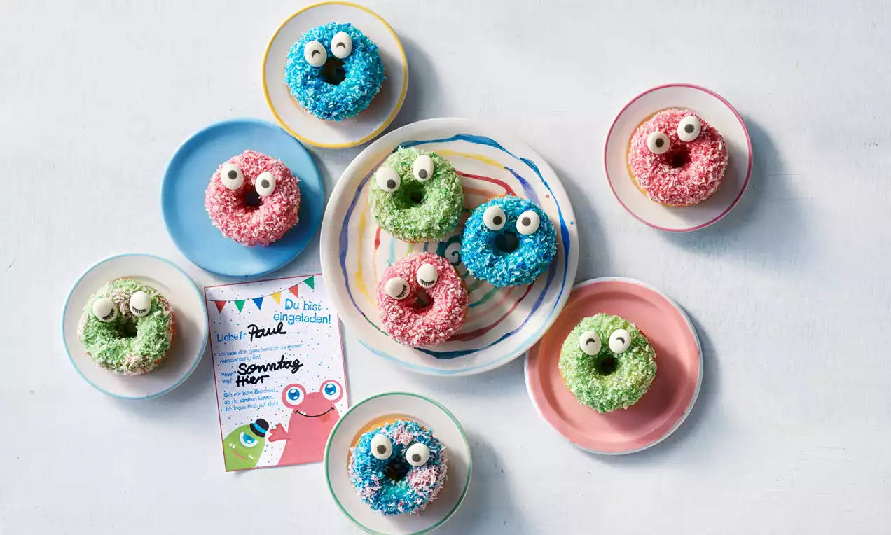 Ein orangefarbener Donut mit gezackter Glasur und dekorativen grünen und schwarzen Elementen liegt auf einem hellen Untergrund