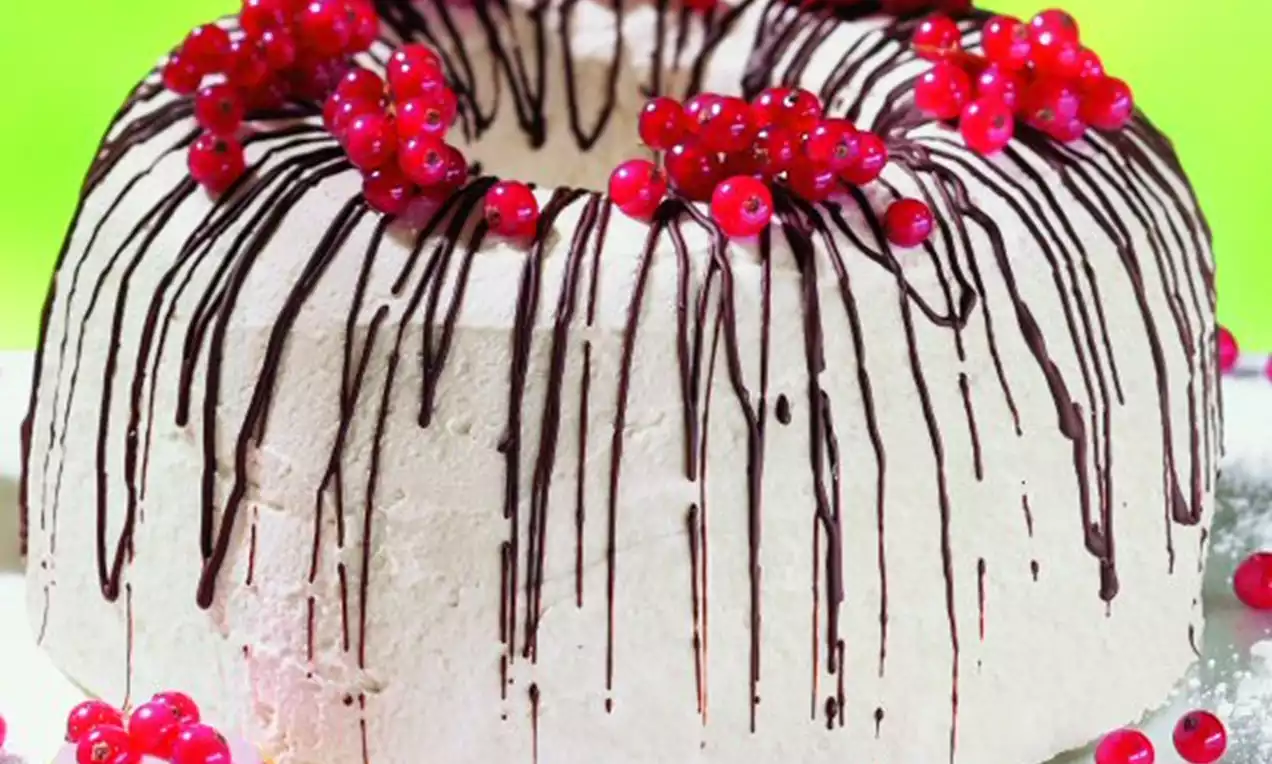 Luftiger Sahnekranz mit Schokoladenstreifen und roten Johannisbeeren als Kranz dekoriert auf weißem Teller mit verstreuten Beeren