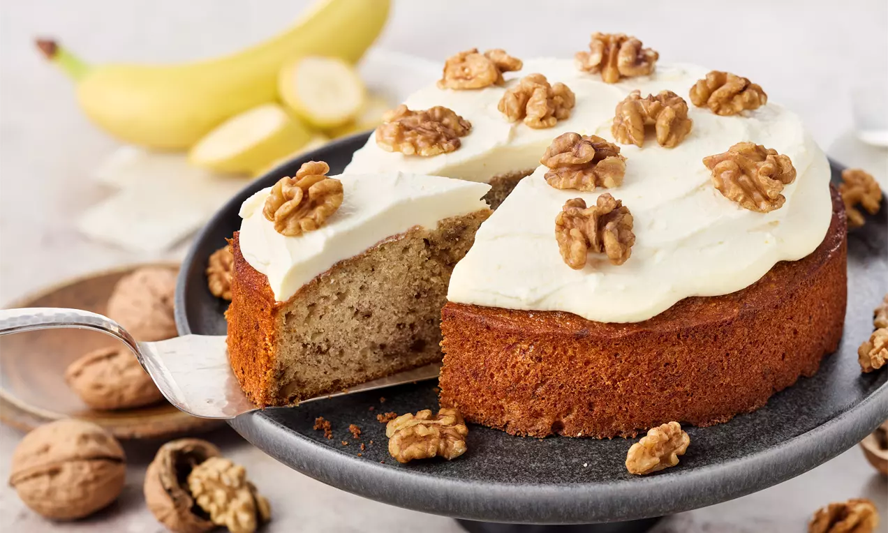 Saftiger Banana Cake in runder Springform mit cremigem Frischkäse-Topping, dekoriert mit halben Walnüssen – einfaches Rezept für Bananenkuchen, schnell gebacken und unwiderstehlich lecker.
