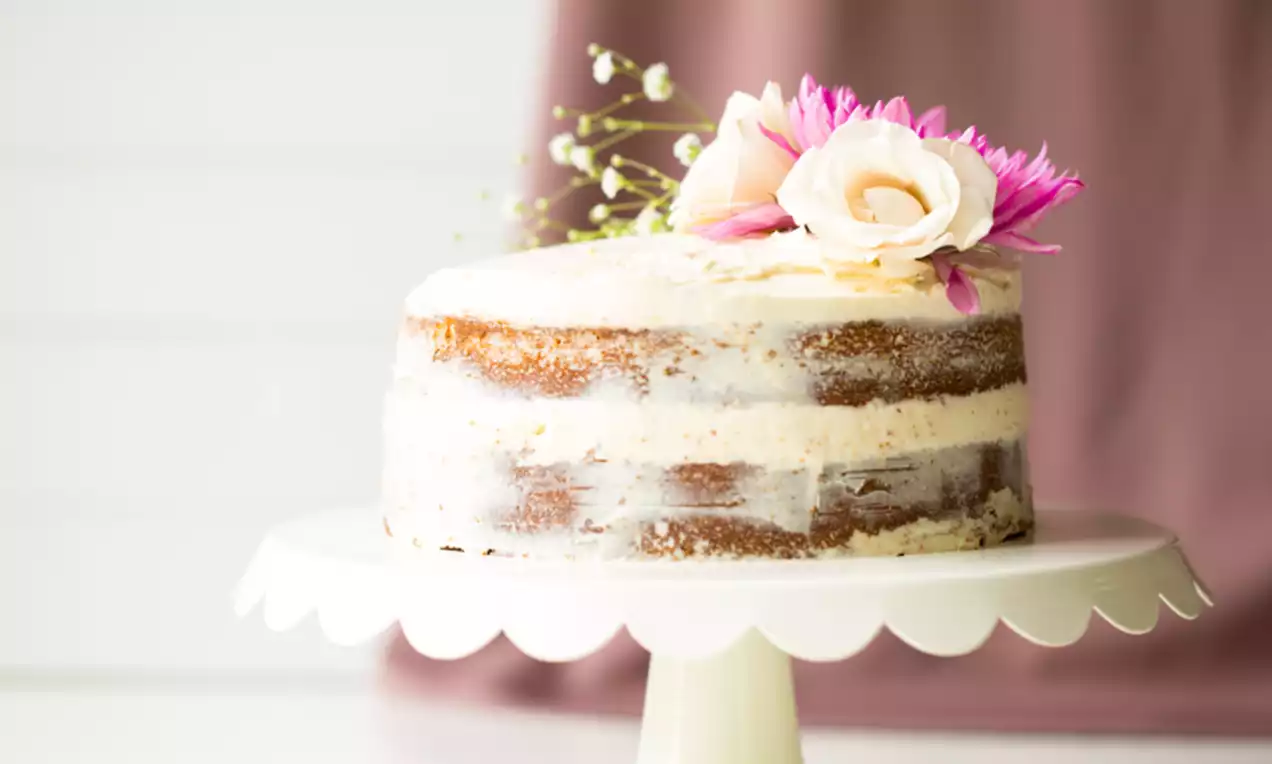 Gâteau Naked Cake aux couches dorées légèrement glacées, couronné de fleurs roses et blanches sur un présentoir blanc élégant