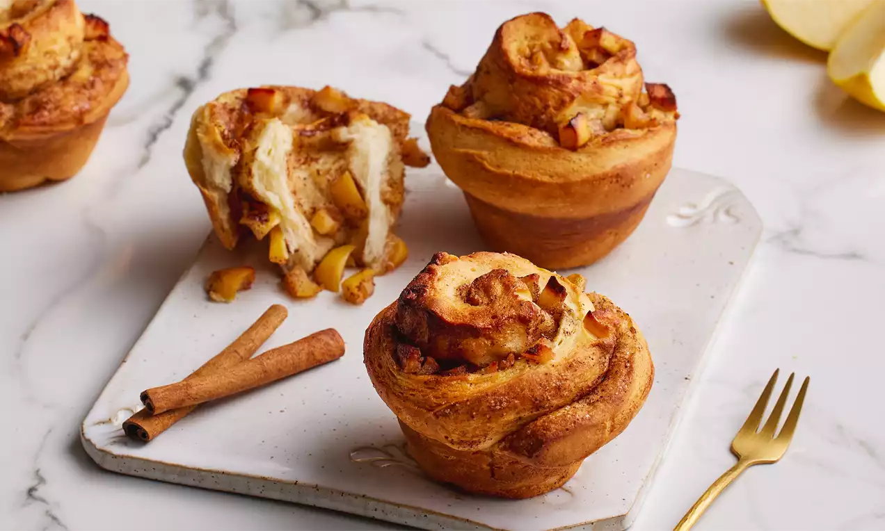 Altın rengi ve kıvrımlı ayvalı rulolar, mermer masada beyaz tabak üzerinde tarçın çubukları ve altın rengi çatal ile düzenlenmiş