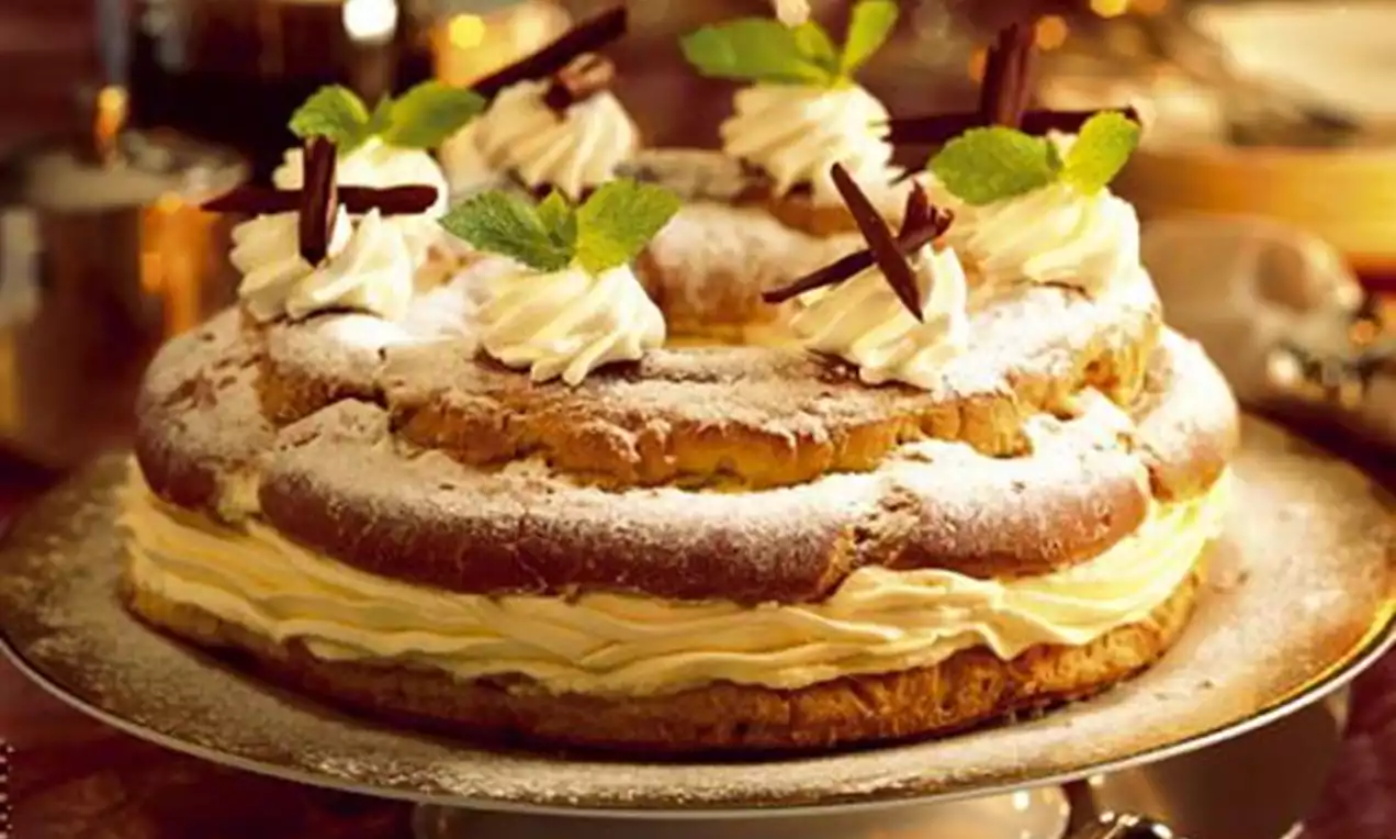 Couronne dorée de pâte légère garnie de crème onctueuse, saupoudrée de sucre glace, décorée de chantilly, copeaux de chocolat et feuilles de menthe