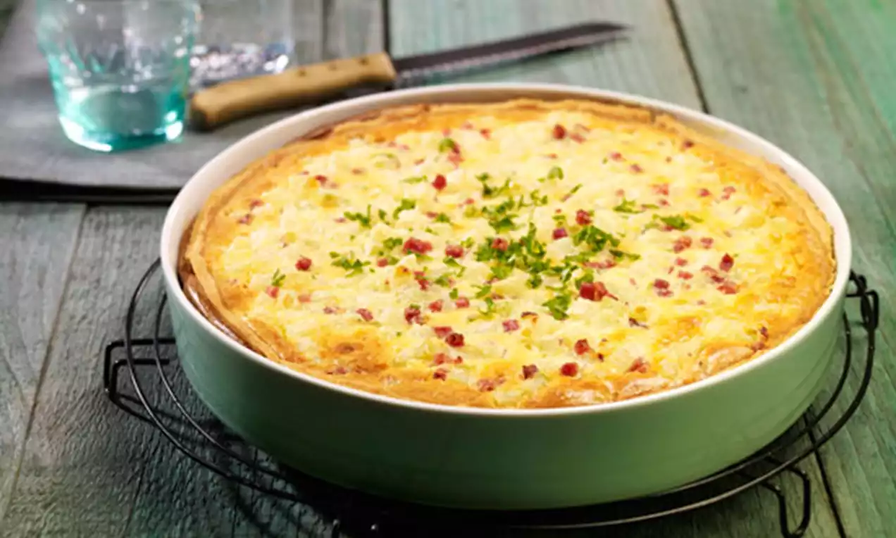 Goldbraune Kohlrabiquiche mit gelblich-cremiger Füllung, roten Speckwürfeln und grünem Petersilienhauch in einer grünen Schale auf Metallgitter