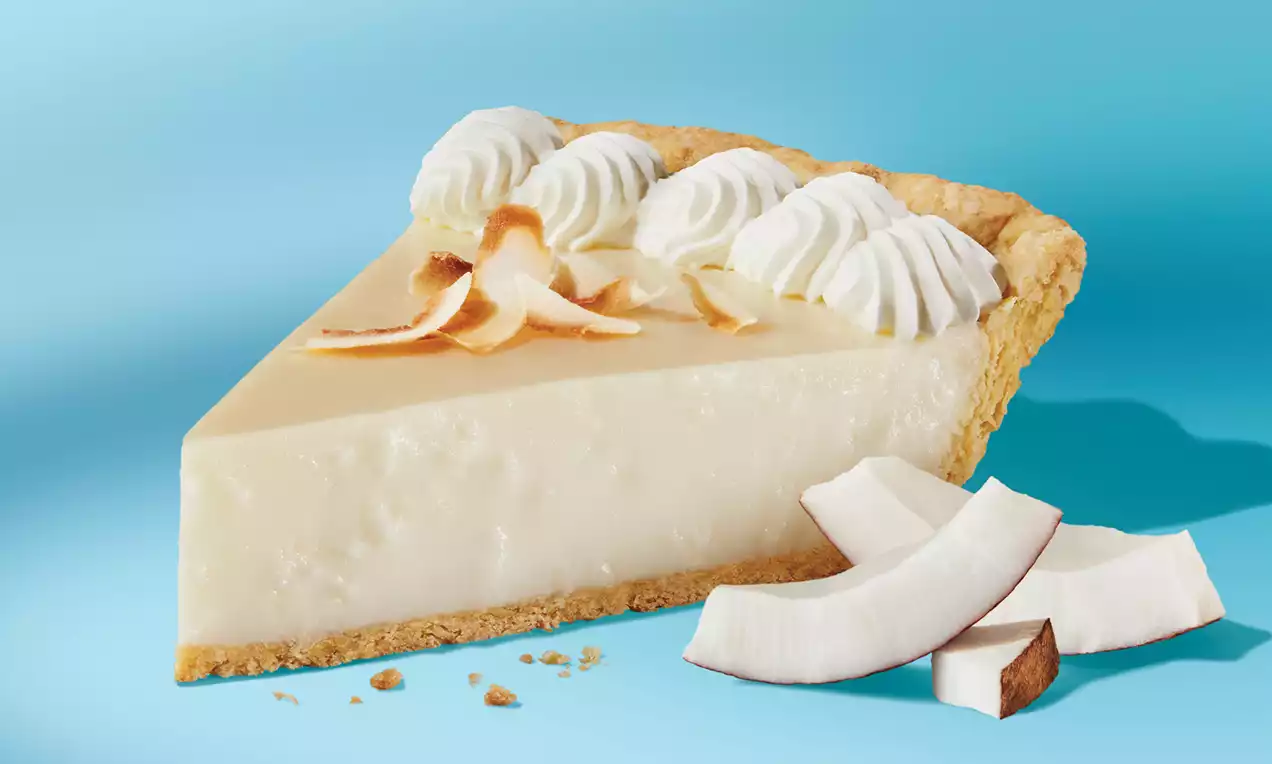 Part de tarte noix de coco à base dorée croustillante avec garniture crémeuse ivoire, chantilly blanche et éclats de coco sur fond bleu