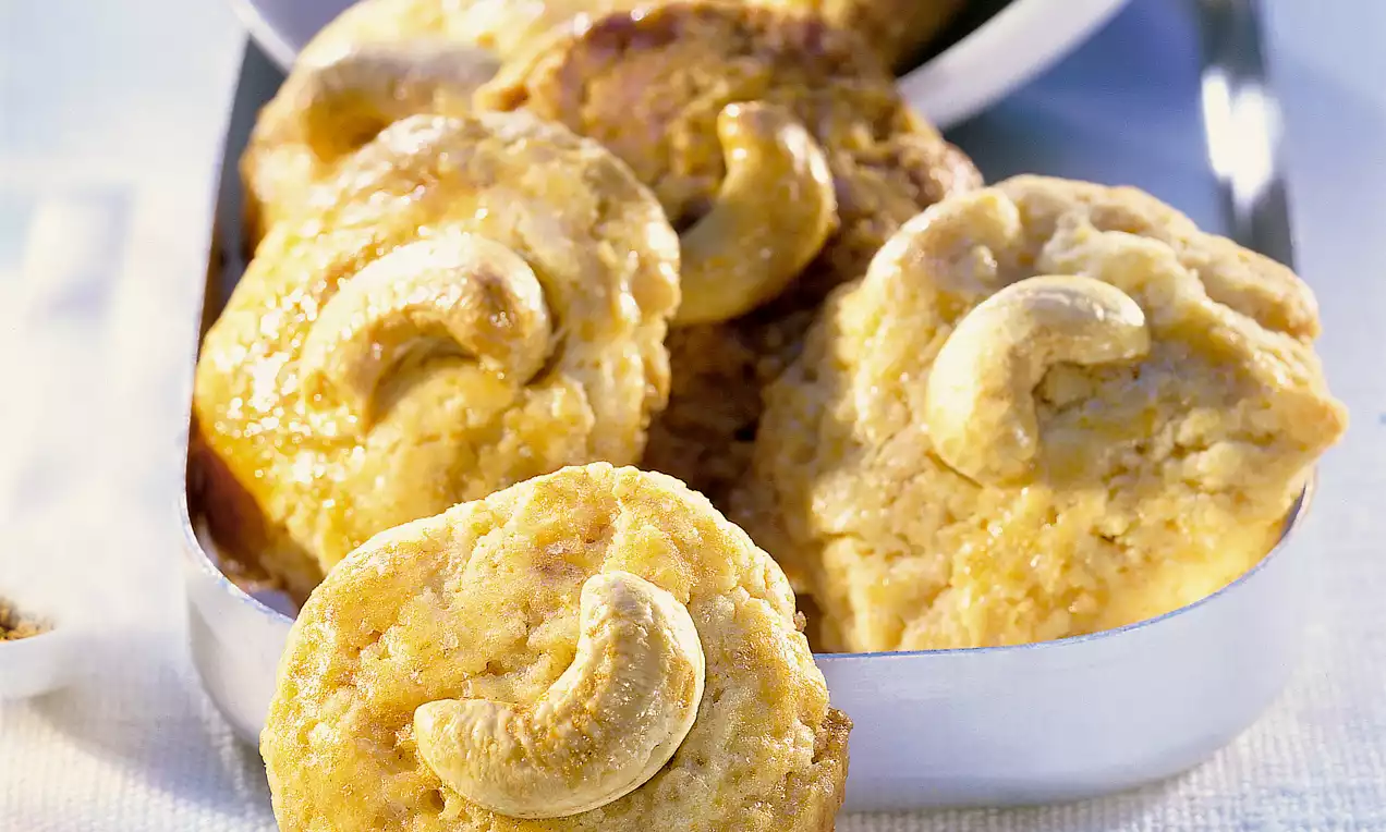 Goldgelbe, runde Cashew-Snacks mit knackigen Cashewkernen in der Mitte, angerichtet in einer silbernen Schale auf hellem Untergrund