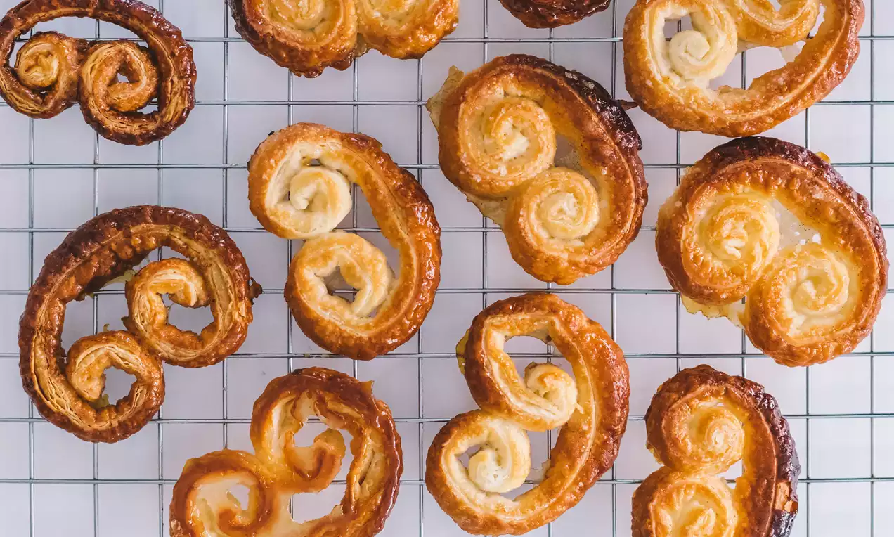 Palmeritas doradas y brillantes con forma de espiral simétrica, borde caramelizado y hojaldre laminado sobre una rejilla metálica