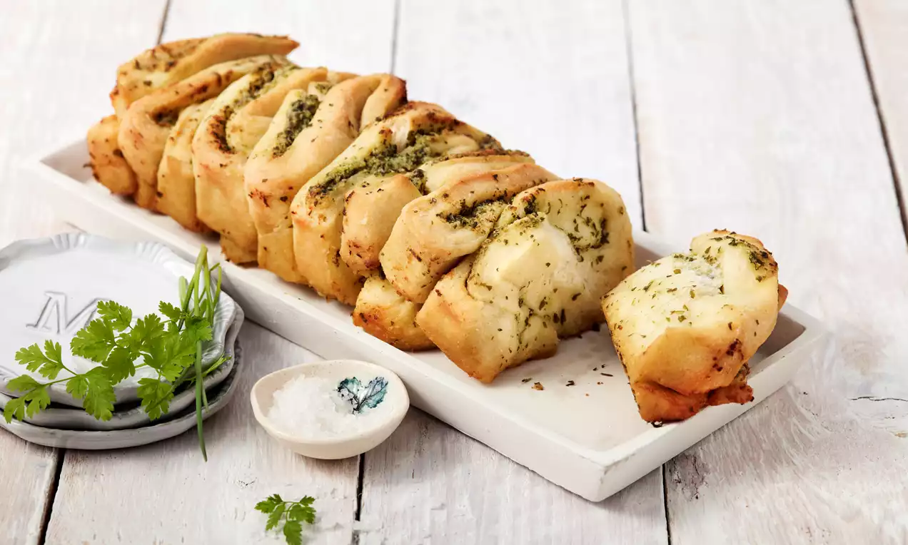 Kräuterzupfbrot mit goldbrauner Kruste und grünen Kräutern, zupfbare Stücke mit butterglänzender Füllung auf Holzbrett serviert
