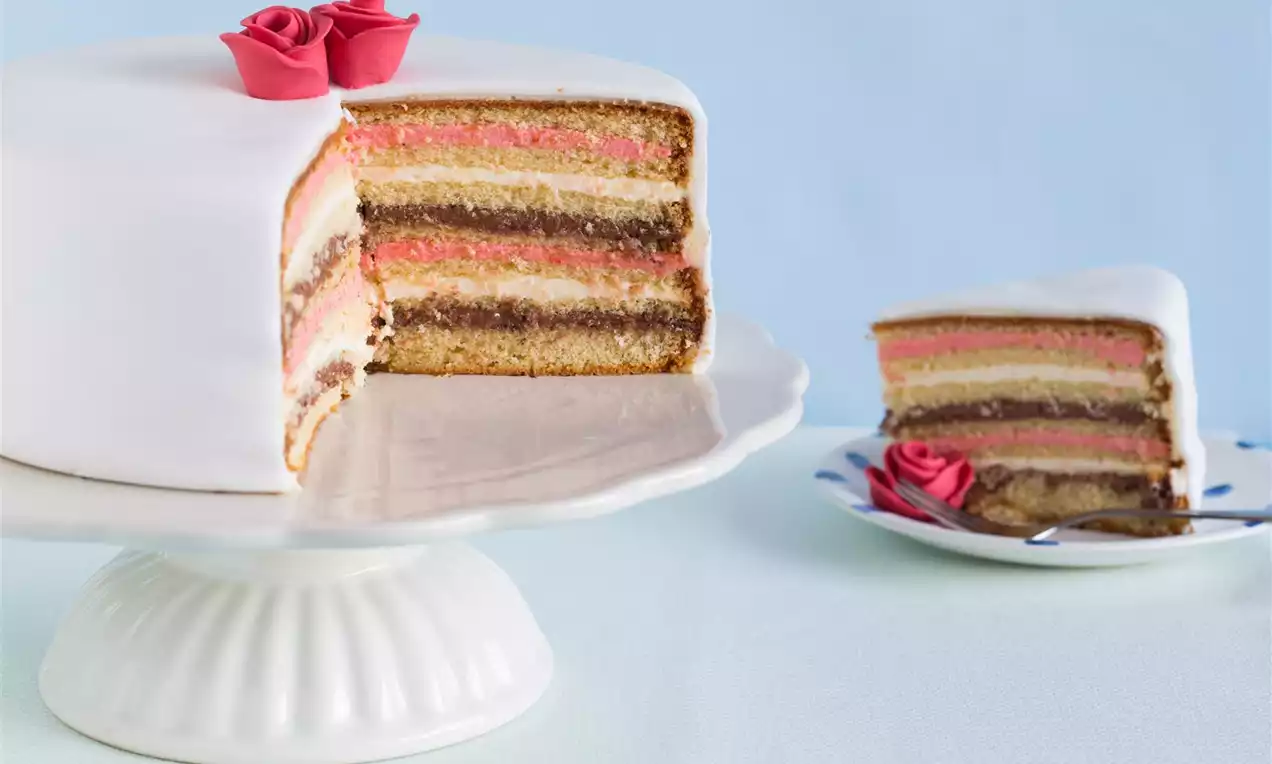 Laagjestaart met witte glazuurlaag, kleurrijke roze en bruine binnenlagen, gedecoreerd met rode suikerrozen op een witte taartschaal