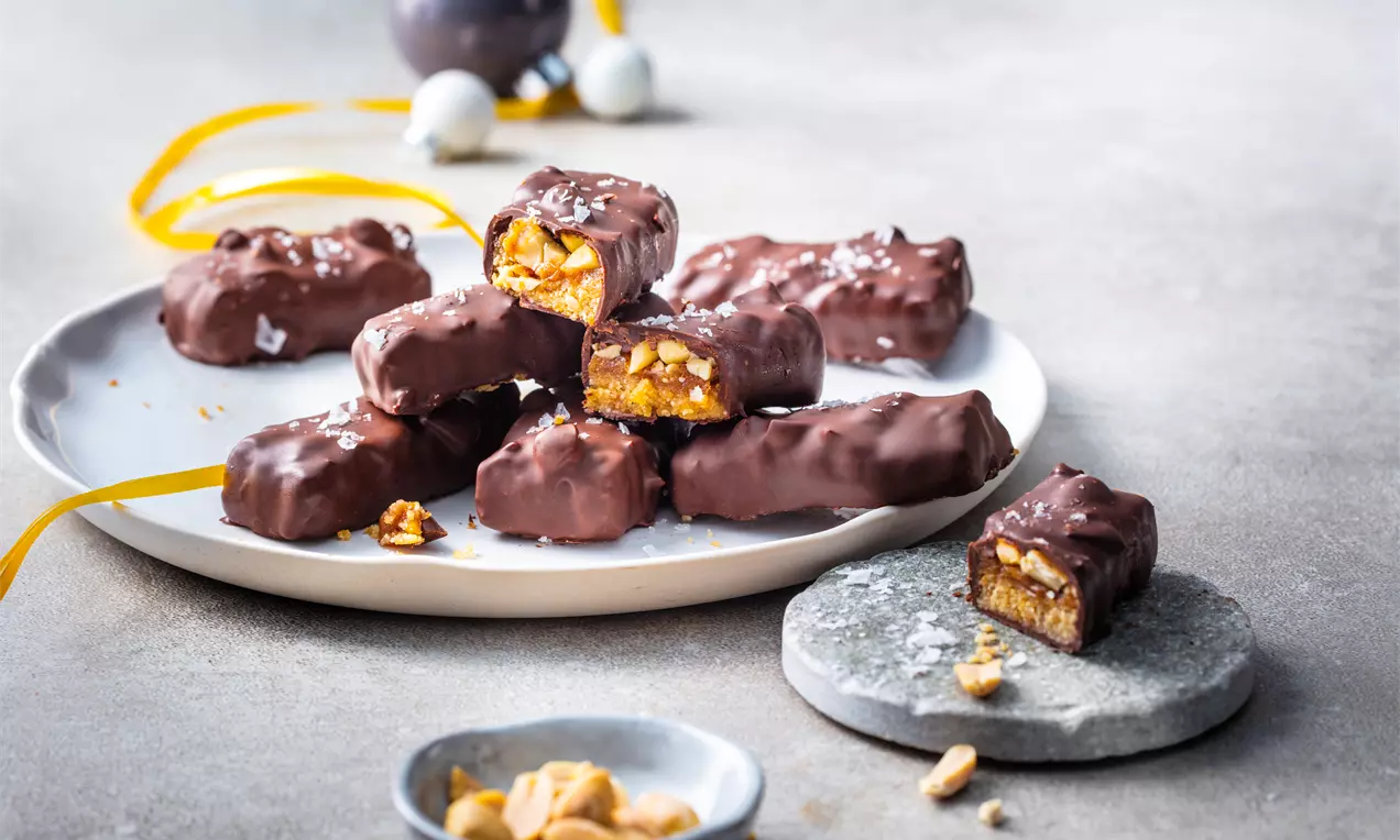 Шоколадови блокчета с неравна глазура, разчупени на парчета, с карамел и ядки вътре, подредени върху бяла чиния и каменна плочка