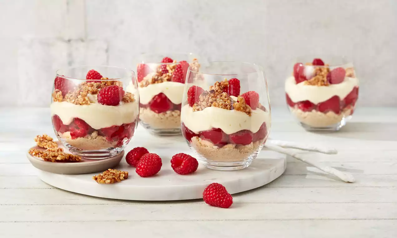 Frankfurter Kranz-Dessert in klaren Gläsern mit hellgelber Creme, roten Himbeeren, knusprigen Krokantstückchen und hellem Keksboden