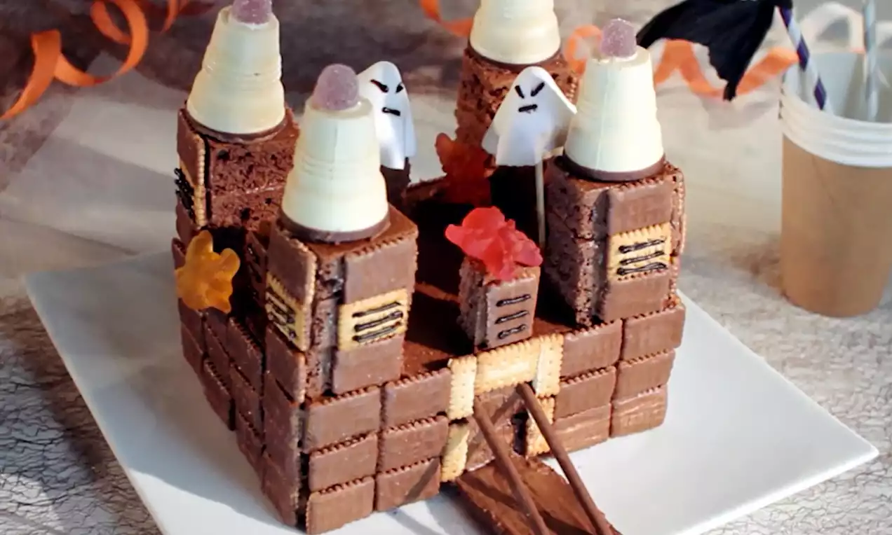 Château en biscuits et chocolat avec tourelles en cônes garnies, décoré de fantômes en sucre et gélatines colorées sur une assiette blanche