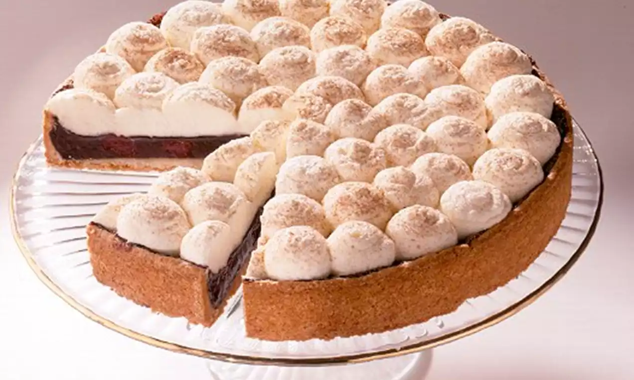 Dornfelder-Kirschkuchen mit braunem Mürbeteigboden, roter Kirschfüllung und Sahnetupfen mit Zimtschicht auf einer gläsernen Tortenplatte