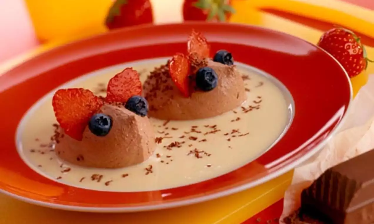 Twee bolletjes luchtige chocolademousse in de vorm van muisjes, versierd met aardbei-oren en blauwe bessen op een lichte saus