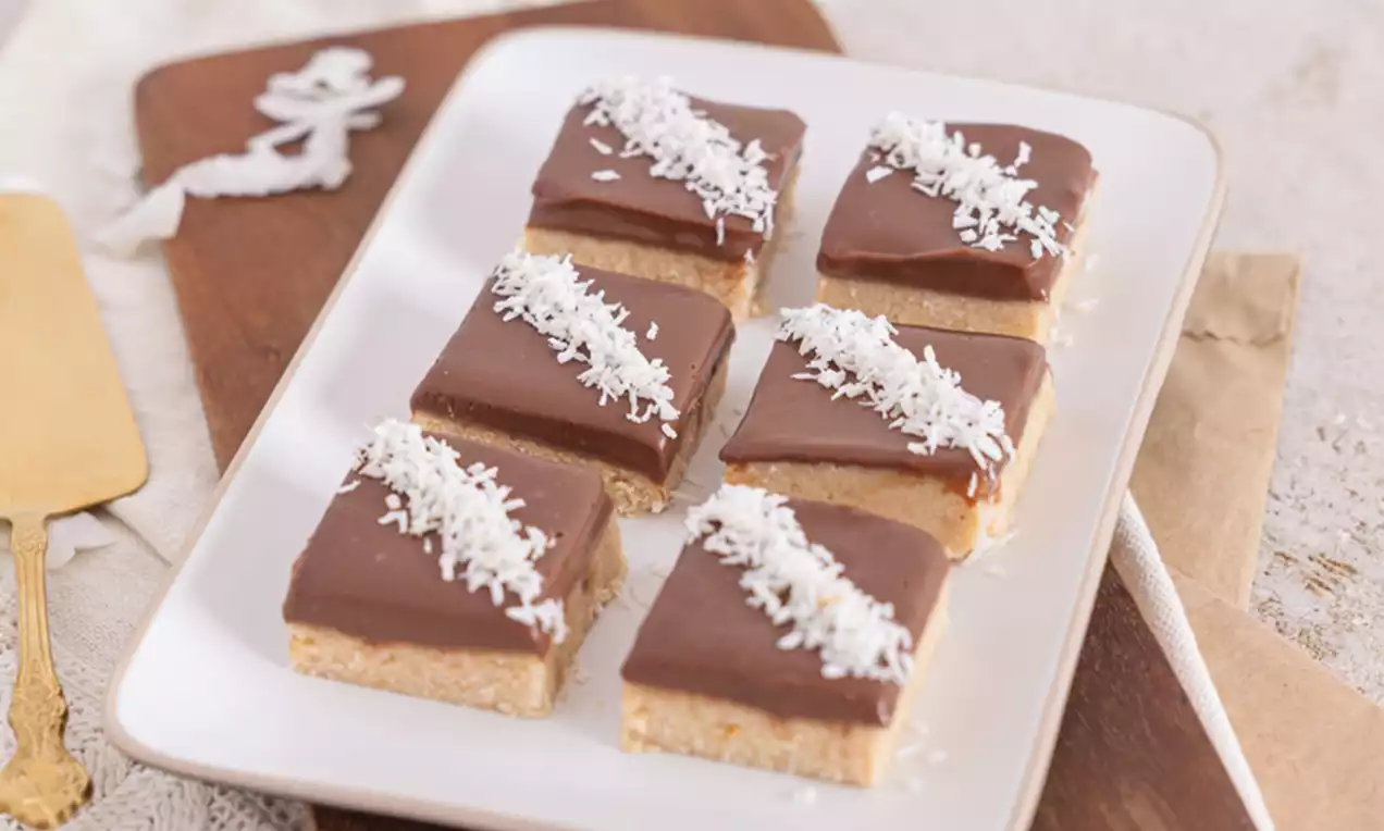 Čokoladne rezine z enakomerno naneseno čokoladno glazuro, posute s tankimi trakci sveže naribanega kokosa, nežno postavljene na bel pravokoten krožnik