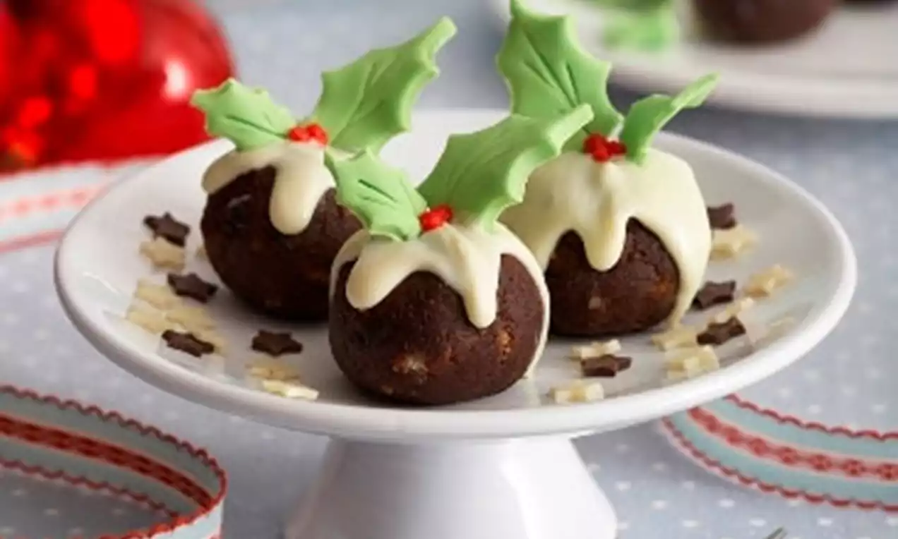 Petits gâteaux ronds chocolatés recouverts de glaçage blanc et décorés de feuilles en sucre vertes et de baies rouges, disposés sur un plat blanc