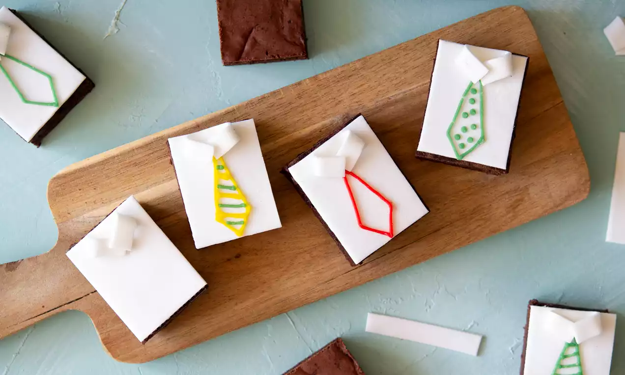 Bruine rechthoekige brownies met witte fondantlaag en kleurrijke strikvormige decoraties, gepresenteerd op een houten plank