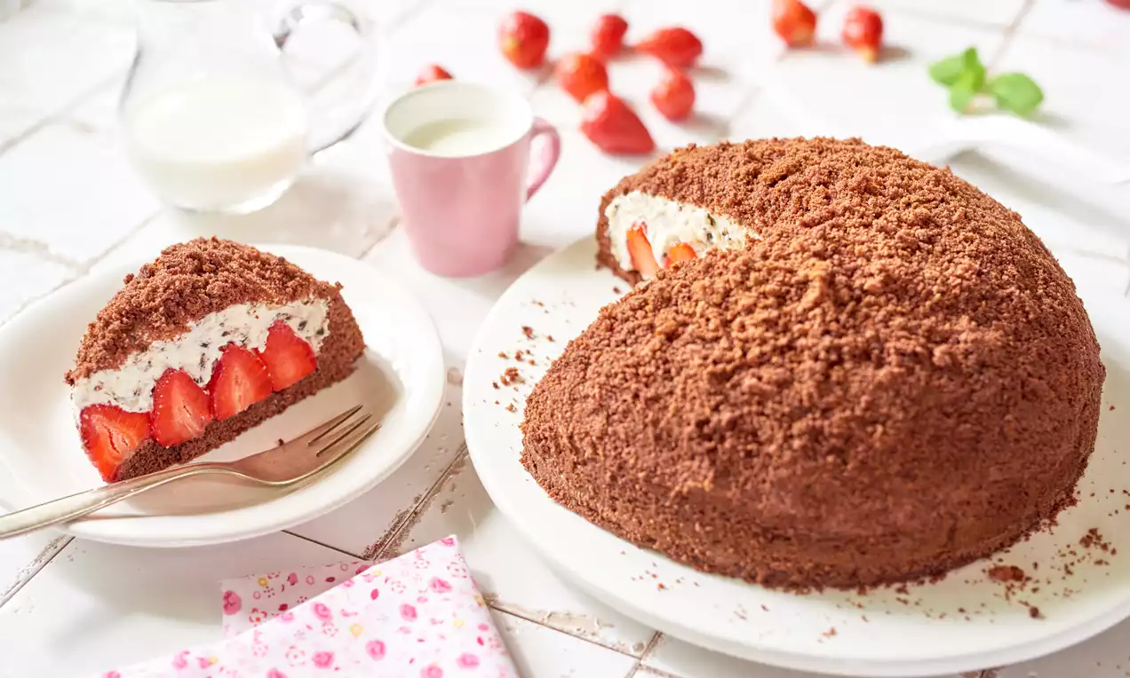 Kopiec z ciemnego, wilgotnego ciasta o nieregularnej strukturze, wypełniony kremem śmietankowym z całymi truskawkami na białym talerzu