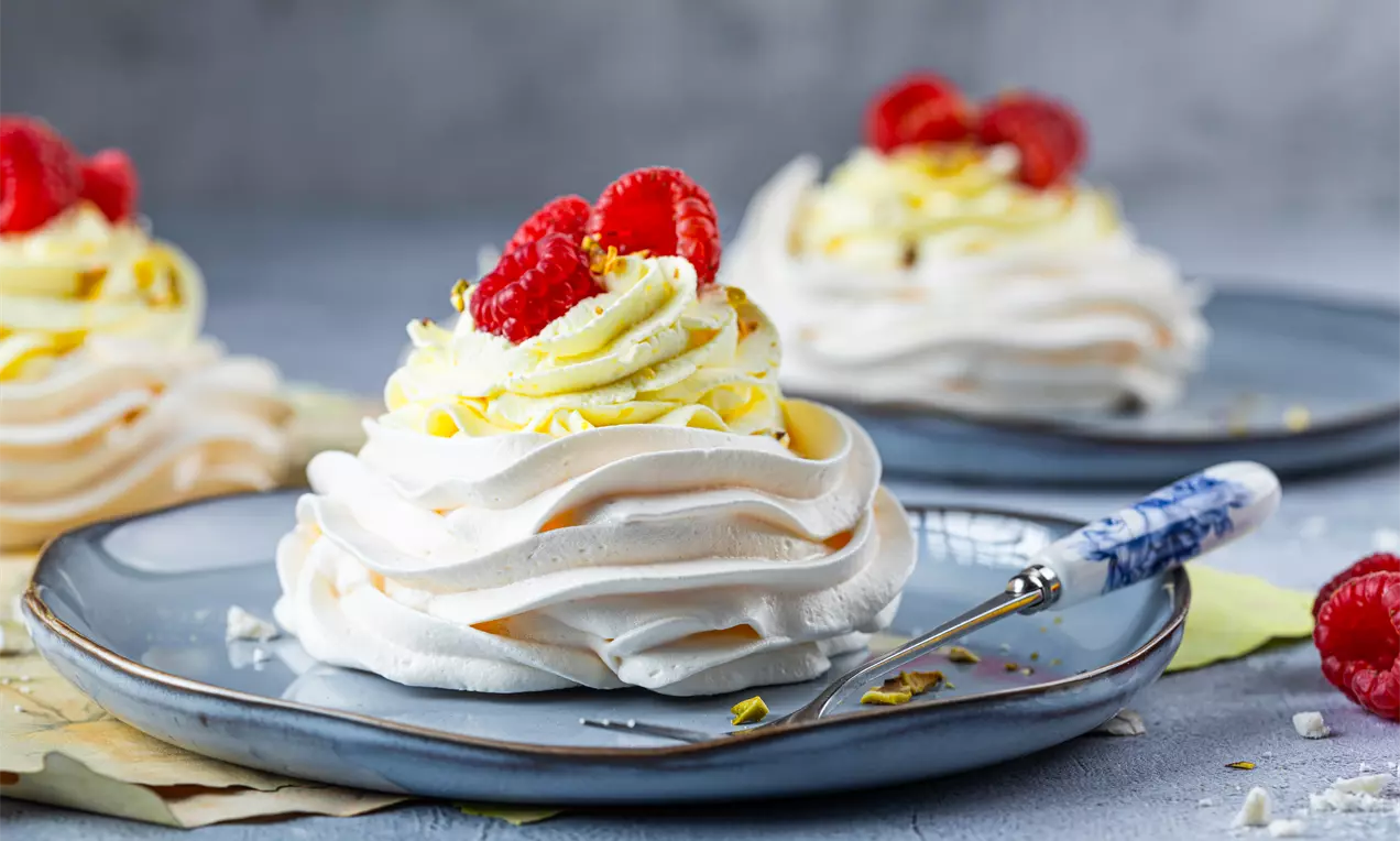 Zdjęcie przedstawia Wiosenne gniazdka bezowe z bitą śmietaną i malinami