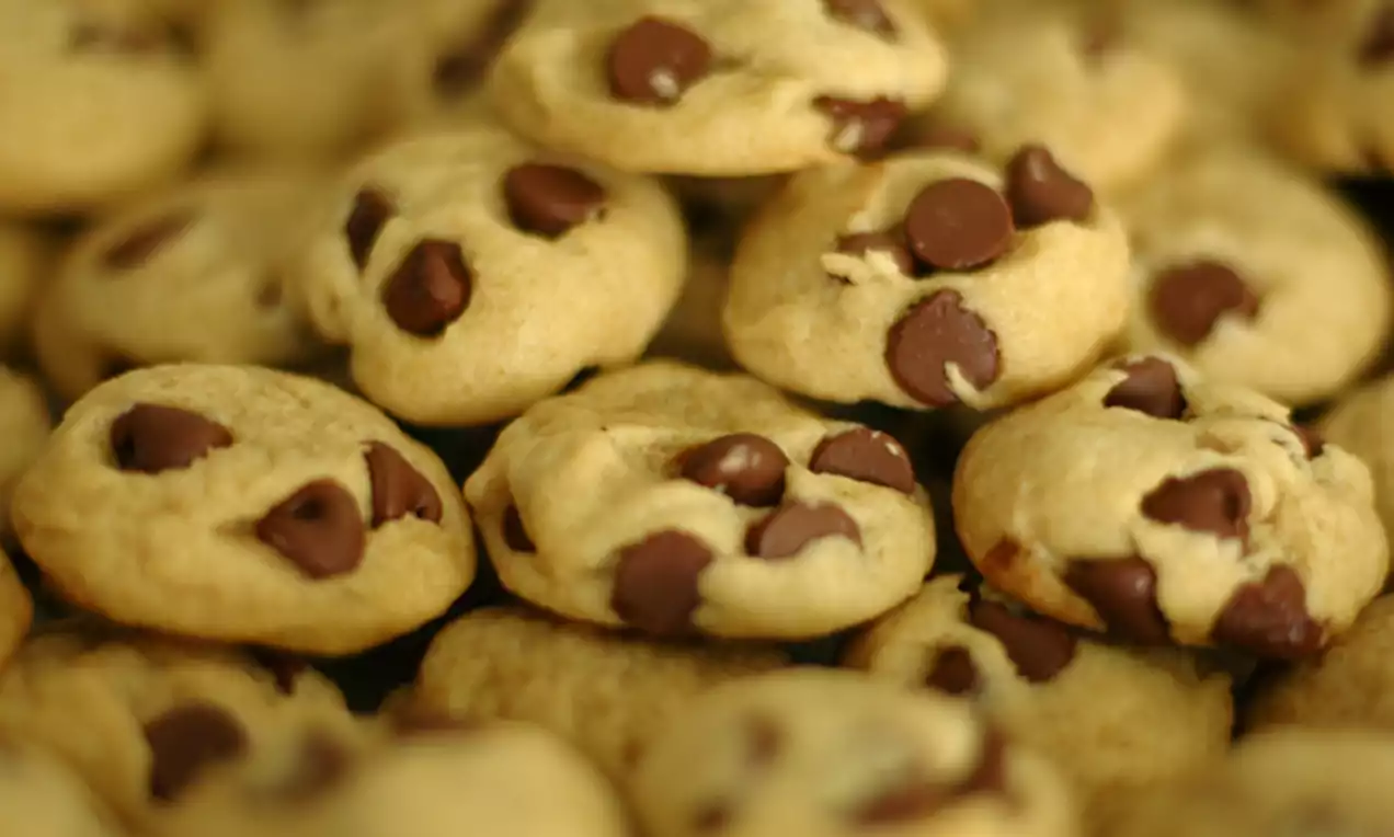 Golden brown cookies with soft, rounded shapes, dotted with glossy chocolate chips, arranged closely together in a warm, textured pile