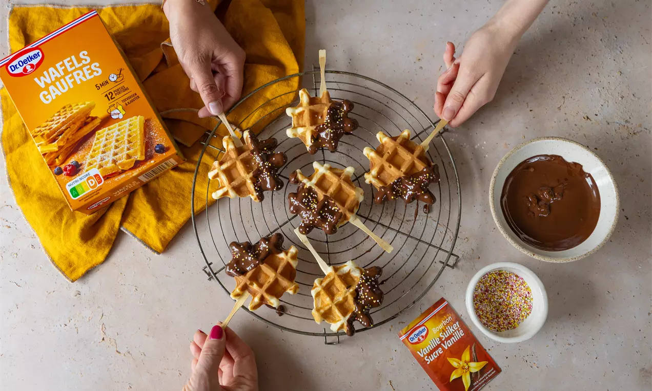 Goudbruine wafel lolly’s gedoopt in gesmolten chocolade en versierd met hagelslag op een metalen koelrek met kleurrijke decoratie