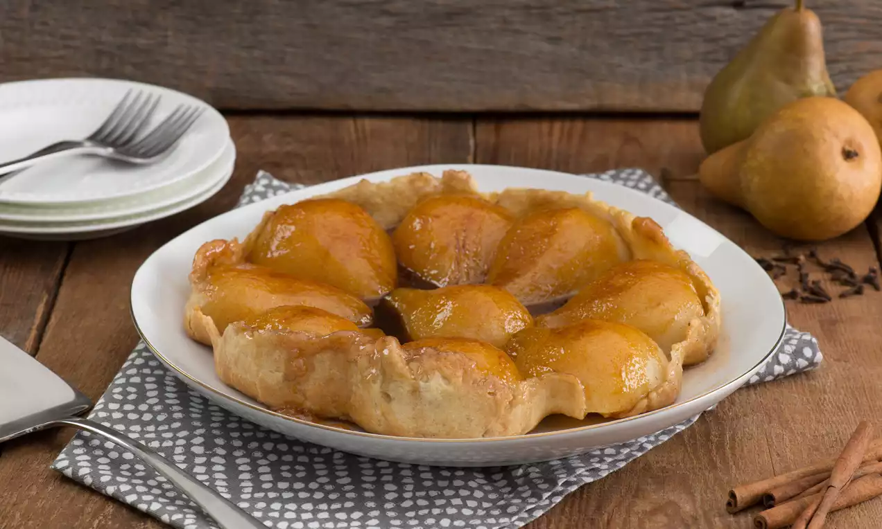Tarte renversée dorée aux poires caramélisées brillantes, disposées sur une pâte croustillante dans une assiette blanche sur une nappe à motifs