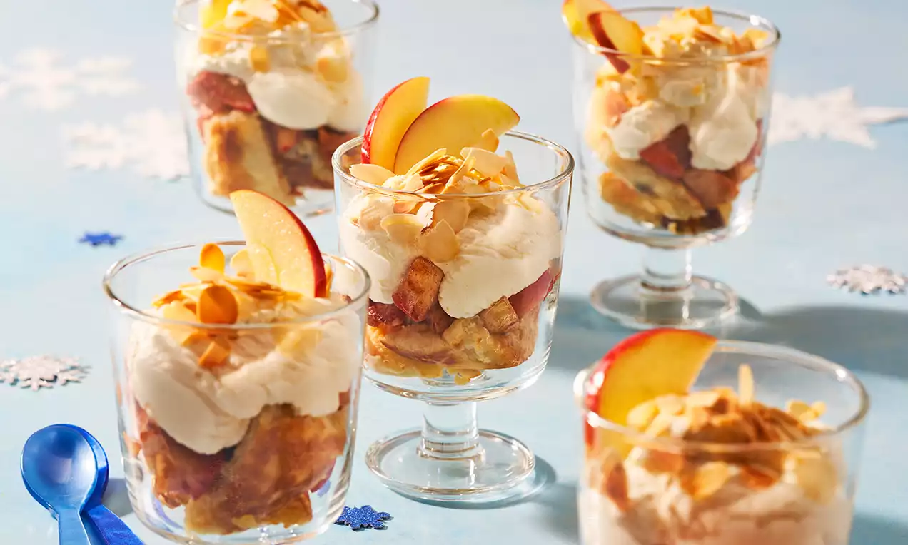 Glazen gevuld met goudbruine Kaiserschmarrn, roomwitte slagroom, dunne appelpartjes en geroosterde amandelen op een lichtblauw tafereel