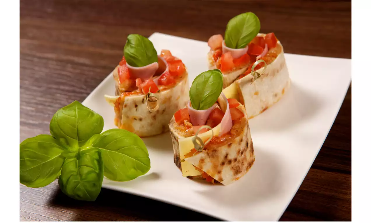 Gefüllte Pizzaspiralen aus goldbraunem Teig mit roter Tomatenfüllung, grünen Basilikumblättern und Holzspießen auf weißem Teller