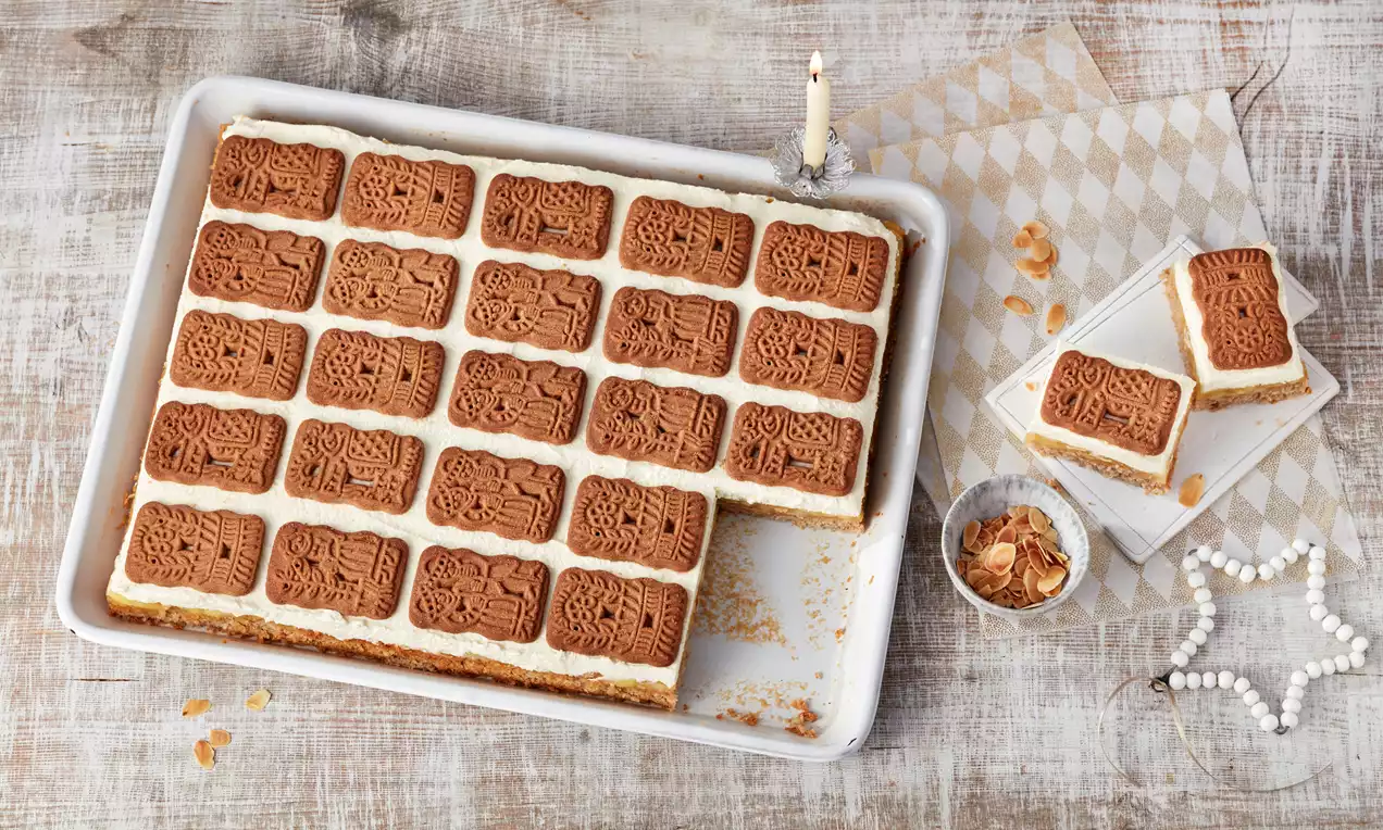 Spekulatius-Kuchen mit goldbraunem Mandelbiskuit, saftiger Apfelfüllung, cremiger Sahne und knusprigen Spekulatiusbröseln auf Teller