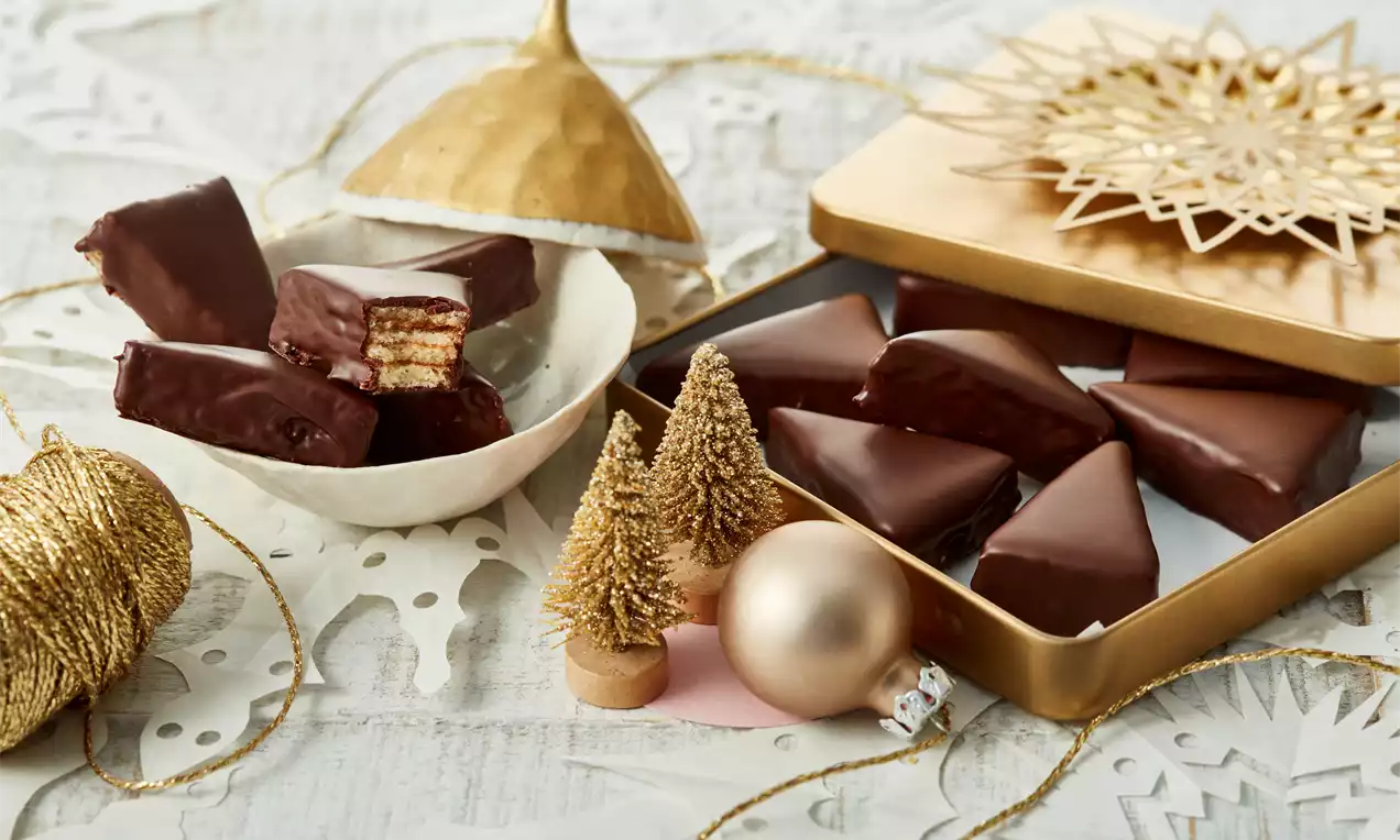 Baumkuchenspitzen in dreieckigen Stücken mit goldbraunen Schichten, dunkler Schokoladenglasur und gehackten Haselnüssen auf weißem Teller