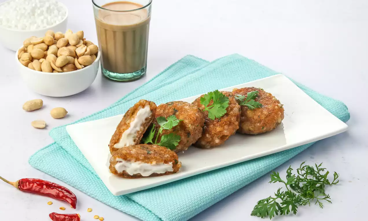 Golden-brown round vadas with a crispy texture, stuffed with creamy white filling, garnished with cilantro on a white rectangular plate