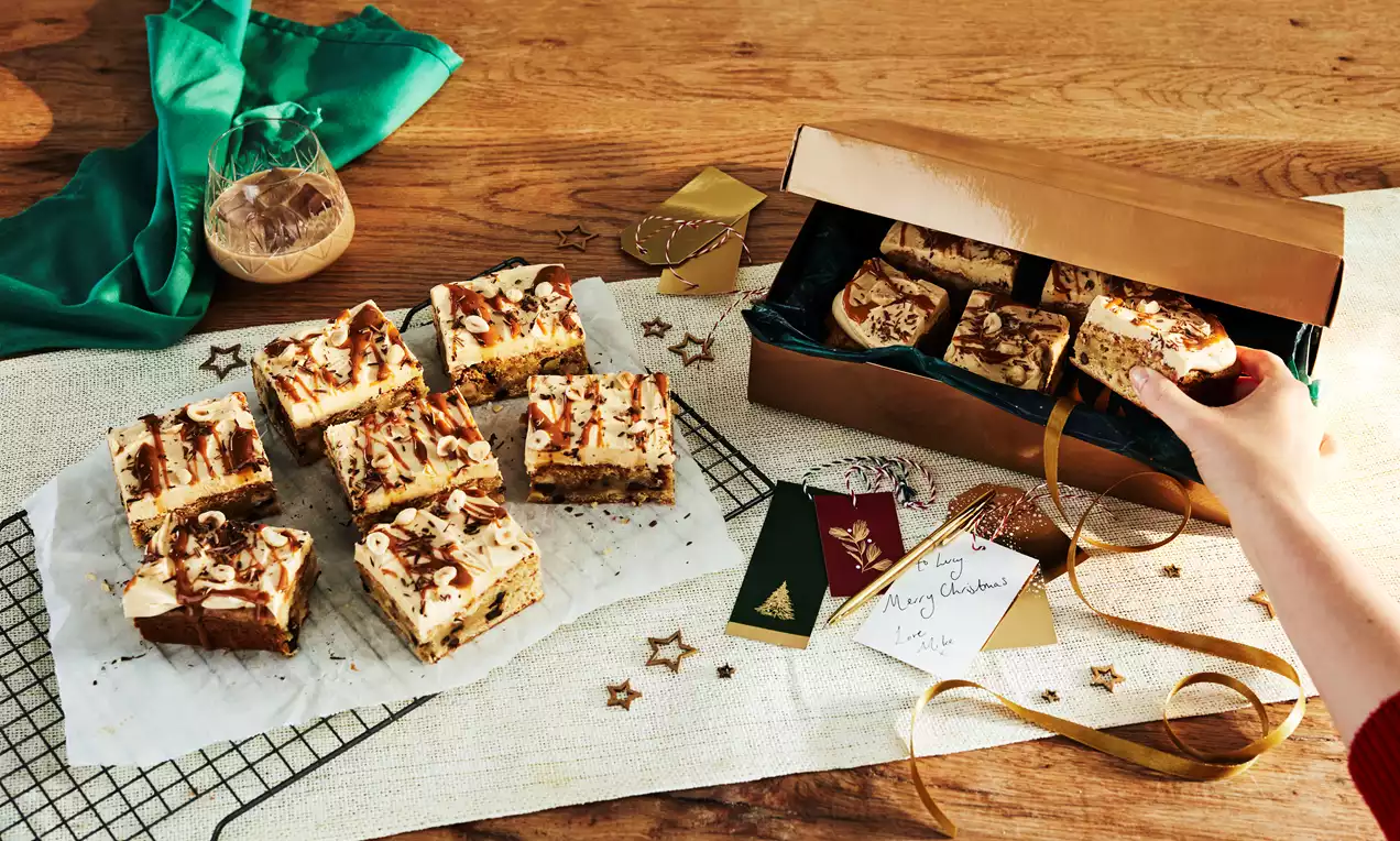 Squares of creamy Baileys cheesecake with a marbled chocolate top and biscuit base, arranged on parchment with festive decor on wood