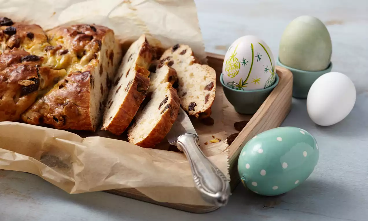Pletenica zlato rjave barve z mehko, rahlo narezano sredico, posuta z rozinami in mandljevimi listi, postrežena na rjavem papirju z okrasnimi jajci