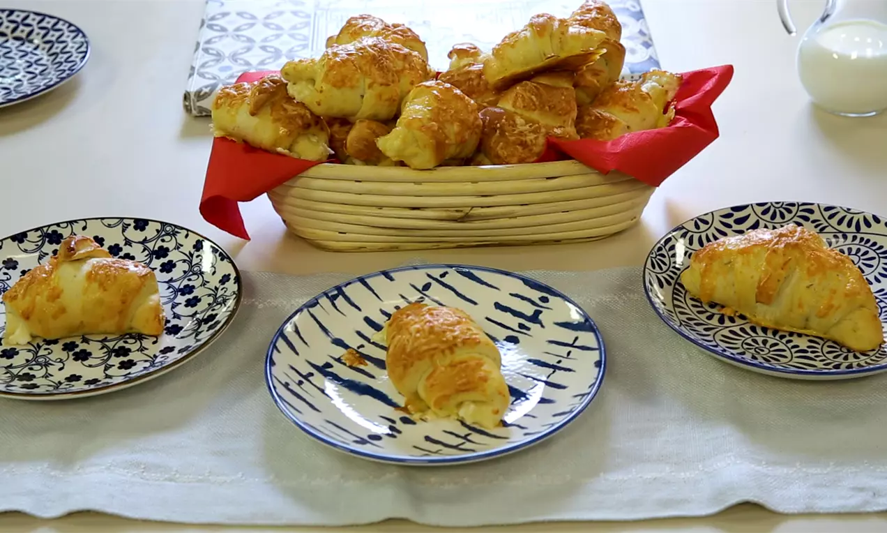 Златисти кифлички с крехка текстура, леко извити, с разтопен сиренен пълнеж, поднесени върху шарени чинии и кош с червена кърпа