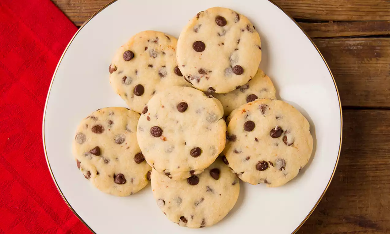 Galletas redondas de shortbread doradas y suaves con chips de chocolate oscuro distribuidas uniformemente sobre un plato blanco sobre madera