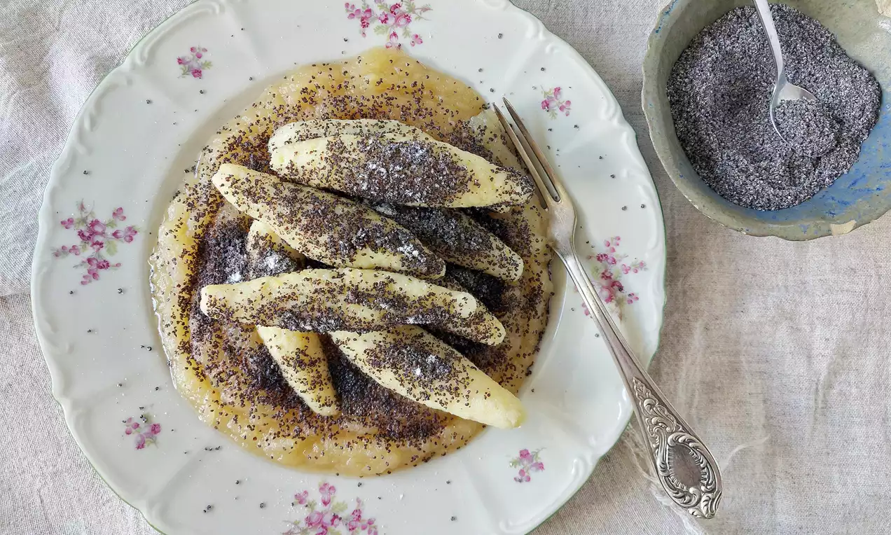 Šulánky světle zlaté barvy, podlouhlého tvaru, posypané tmavým mákem na hladké jablečné omáčce, servírované na květovaném talíři